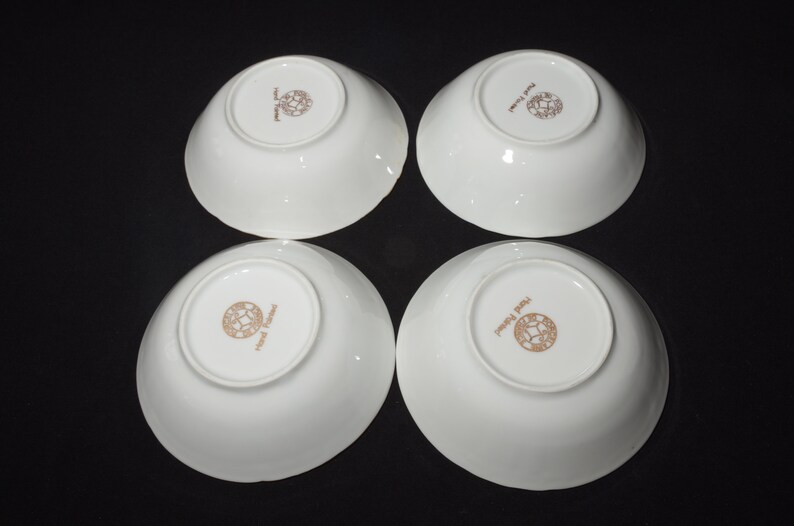 May include: Four white ceramic bowls with a gold rim and a gold logo that reads "Royal Delft" on the bottom.