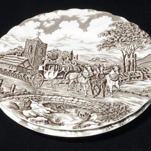 Könnte beinhalten: Set aus drei dekorativen Tellern mit einem sepiafarbenen Transferdruck-Design. Die Teller zeigen eine detaillierte Szene einer Pferdekutsche auf einer Straße, vorbei an einer Kirche und einem Cottage. Die Teller haben einen gewellten Rand.