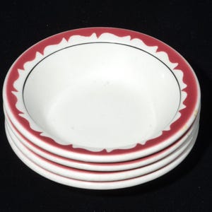 May include: A stack of four small, white ceramic bowls. Each bowl has a decorative red scalloped border and a thin black line. The bowls are stacked on top of each other, with the top bowl showing the interior.