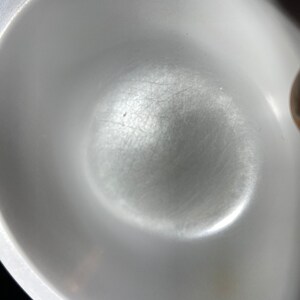 May include: A white ceramic bowl with a smooth, slightly textured surface. The bowl has a slight indentation in the center.