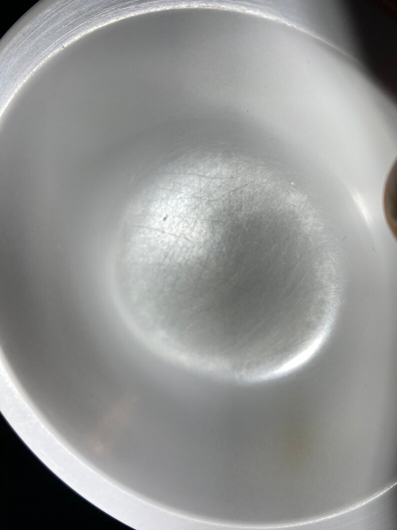 May include: A white ceramic bowl with a smooth, slightly textured surface. The bowl has a slight indentation in the center.