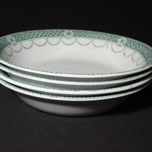 May include: A stack of four white ceramic bowls with a green and white patterned rim. The bowls are stacked on a black surface.