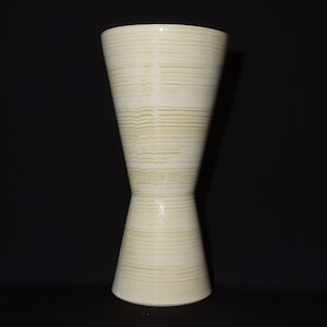 May include: A white ceramic vase with a textured, striped design. The vase has a wide mouth and a narrow base, creating an hourglass shape.