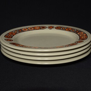 May include: A stack of four white ceramic plates with a brown and orange geometric pattern around the rim.