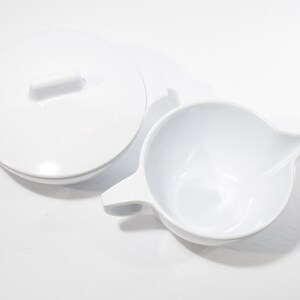 May include: A white ceramic creamer and sugar bowl set. The creamer has a handle and a spout. The sugar bowl has a lid.