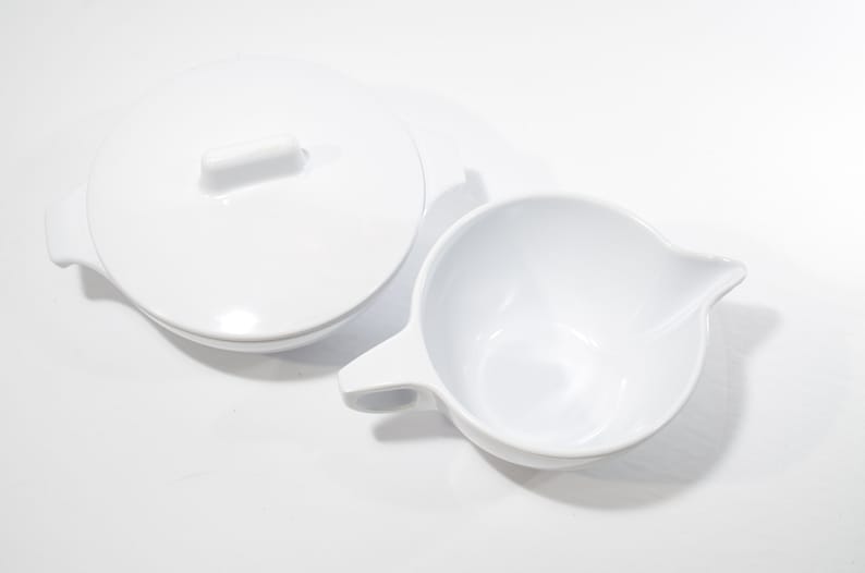May include: A white ceramic creamer and sugar bowl set. The creamer has a handle and a spout. The sugar bowl has a lid.