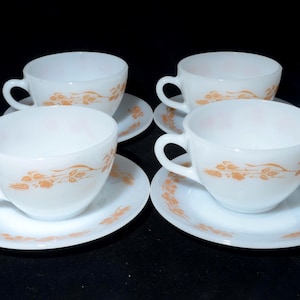 May include: Four white teacups and saucers with a delicate orange floral design. The cups have curved handles and sit on matching saucers. The set is likely vintage and suitable for serving tea or coffee.