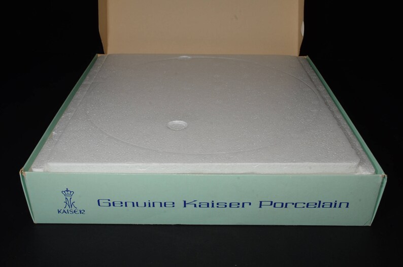 May include: A light blue box with a white foam insert and the text "Genuine Kaiser Porcelain" printed on the front. The box has a crown logo with the word "Kaiser" underneath.
