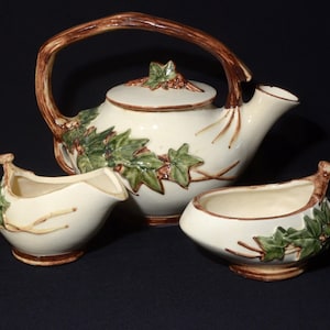 May include: A vintage tea set featuring a teapot, creamer and sugar bowl. The set is decorated with a brown twig design and green ivy leaves.