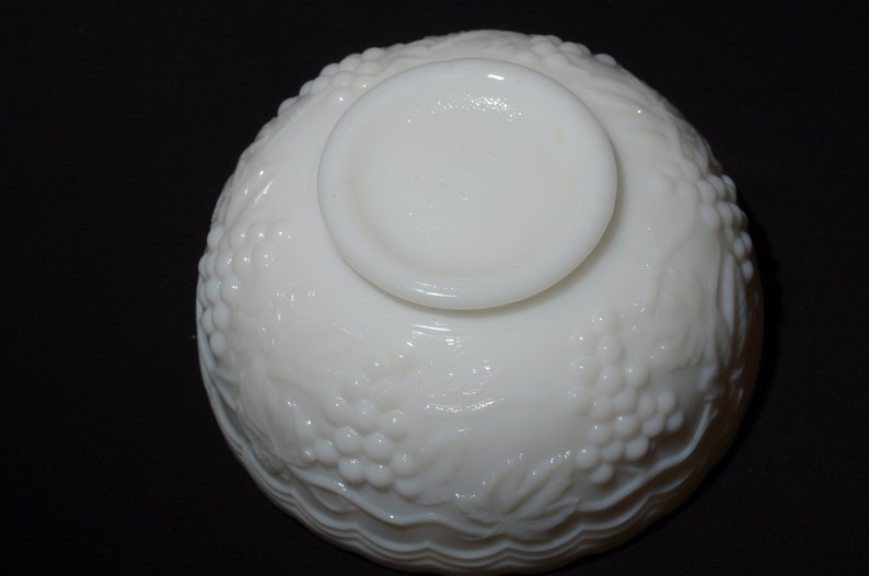 K&ouml;nnte beinhalten: Eine wei&szlig;e Sch&uuml;ssel im Vintage-Stil mit einem erhabenen Trauben- und Bl&auml;ttermuster. Die Sch&uuml;ssel hat einen kreisf&ouml;rmigen Boden und einen abgerundeten K&ouml;rper. Die Unterseite der Sch&uuml;ssel ist sichtbar und zeigt den Boden und das detaillierte Traubendesign. Die Sch&uuml;ssel besteht aus gl&auml;nzendem, undurchsichtigem wei&szlig;em Material.