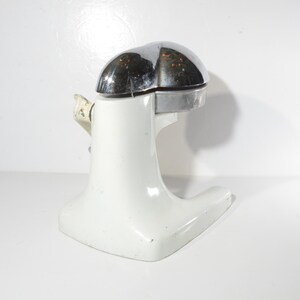 May include: White ceramic citrus juicer with a chrome top. The juicer has a wide base and a narrow spout.