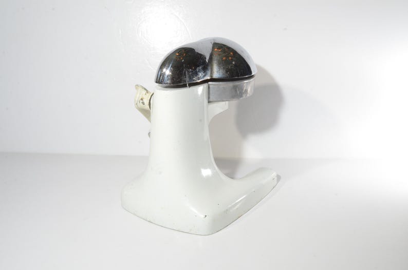 May include: White ceramic citrus juicer with a chrome top. The juicer has a wide base and a narrow spout.