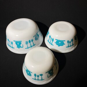 May include: Set of three white ceramic bowls with a blue and white kitchen themed design. The bowls are nested inside each other.