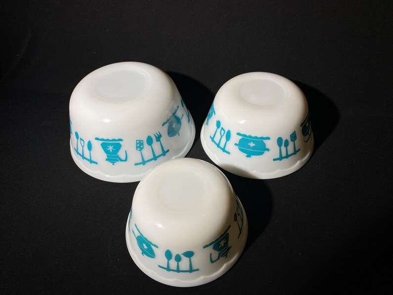 May include: Set of three white ceramic bowls with a blue and white kitchen themed design. The bowls are nested inside each other.