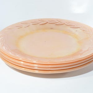 May include: A stack of four peach-colored glass dessert plates with a delicate leaf design around the rim.