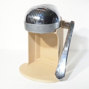 May include: A vintage chrome and beige manual citrus juicer with a lever handle.