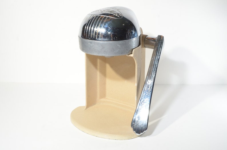 May include: A vintage chrome and beige manual citrus juicer with a lever handle.