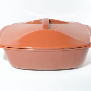 以下が含まれることがあります： 蓋と取っ手がついたテラコッタ色のセラミック製のキャセロール。皿は正方形で、滑らかで光沢のある仕上げです。