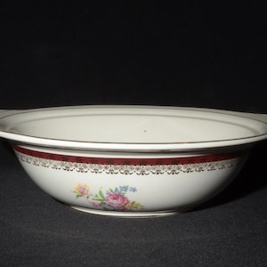 May include: A white oval serving bowl with a red and gold trim and floral design. The bowl has a slightly raised rim and a smooth, glossy finish.