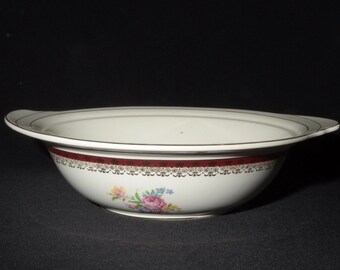 May include: A white oval serving bowl with a red and gold trim and floral design. The bowl has a slightly raised rim and a smooth, glossy finish.