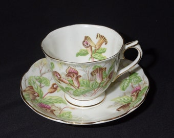Puede incluir: Una taza de té y un platillo blancos con un patrón floral. El patrón presenta flores rosas, marrones y verdes con detalles dorados.