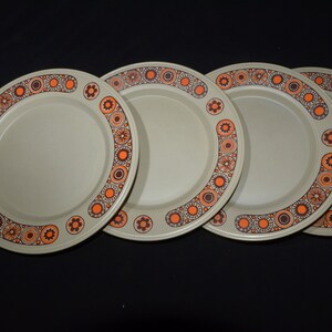 May include: Set of four beige dinner plates with a brown and orange geometric pattern around the rim.