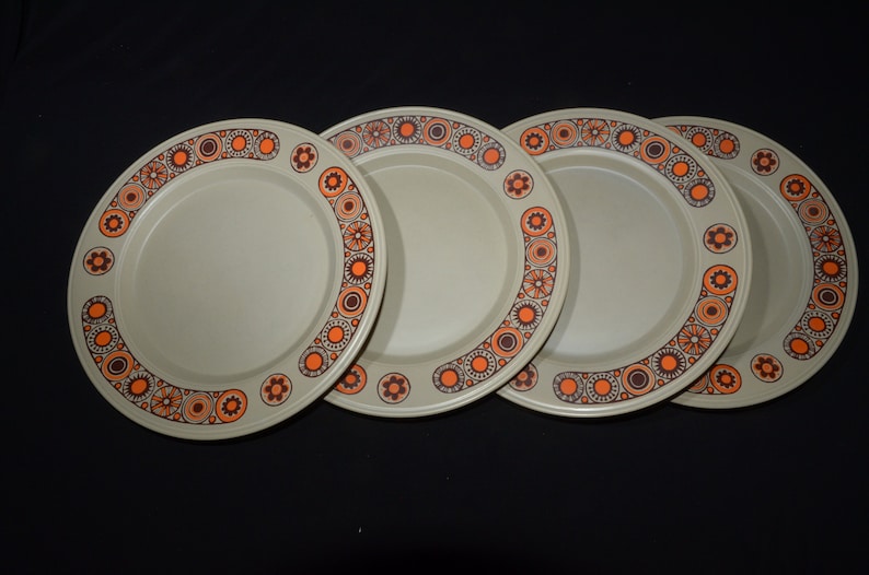 May include: Set of four beige dinner plates with a brown and orange geometric pattern around the rim.
