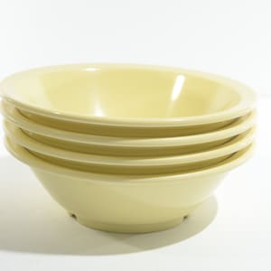 May include: A stack of four pale yellow ceramic bowls. The bowls are stacked on top of each other, with the largest bowl on the bottom and the smallest bowl on top.