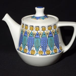 May include: White ceramic teapot with a blue and yellow fish pattern. The teapot has a lid and a handle.