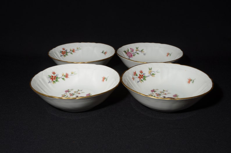 May include: Set of four white porcelain bowls with a gold rim and floral pattern. The bowls are ideal for serving soup, cereal, or dessert.