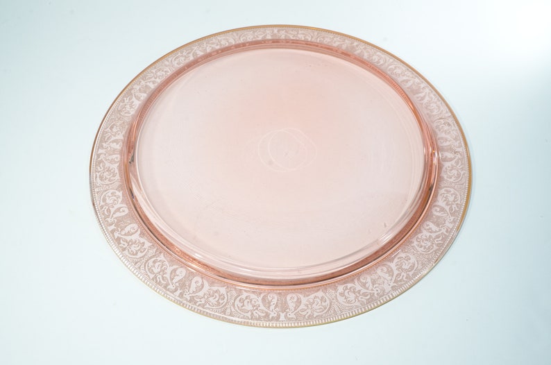 Puede incluir: Una bandeja de servir de vidrio rosa con un borde dorado y un delicado dise&ntilde;o floral grabado.