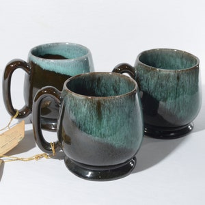 Puede incluir: Tres tazas de cerámica marrón con un esmalte turquesa. Las tazas tienen una forma redondeada y un asa en el lateral.