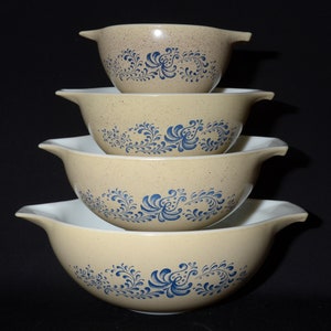 Puede incluir: Un juego de cuatro cuencos para mezclar apilados. Los cuencos son de color beige con un diseño floral azul. Cada cuenco tiene un asa a cada lado. Los cuencos tienen un acabado moteado.