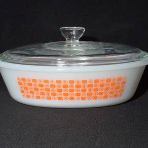 May include: White oval casserole dish with a glass lid. The dish has an orange and white geometric pattern.