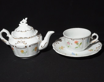 Juego de té Toutant de porcelana fina: tetera individual, taza y platillo con detalles dorados y diseño floral.