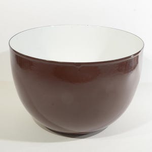 Puede incluir: Un tazón de cerámica marrón con un interior blanco. El tazón es redondo y tiene un acabado liso y brillante.
