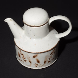 May include: A white ceramic teapot with a brown wheat design. The teapot has a lid and a handle.
