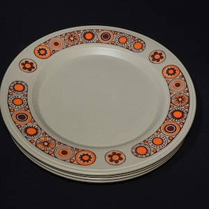 May include: A set of four beige dinner plates with a brown and orange geometric pattern around the rim.