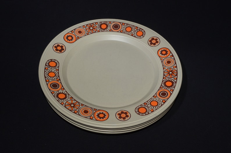 May include: A set of four beige dinner plates with a brown and orange geometric pattern around the rim.