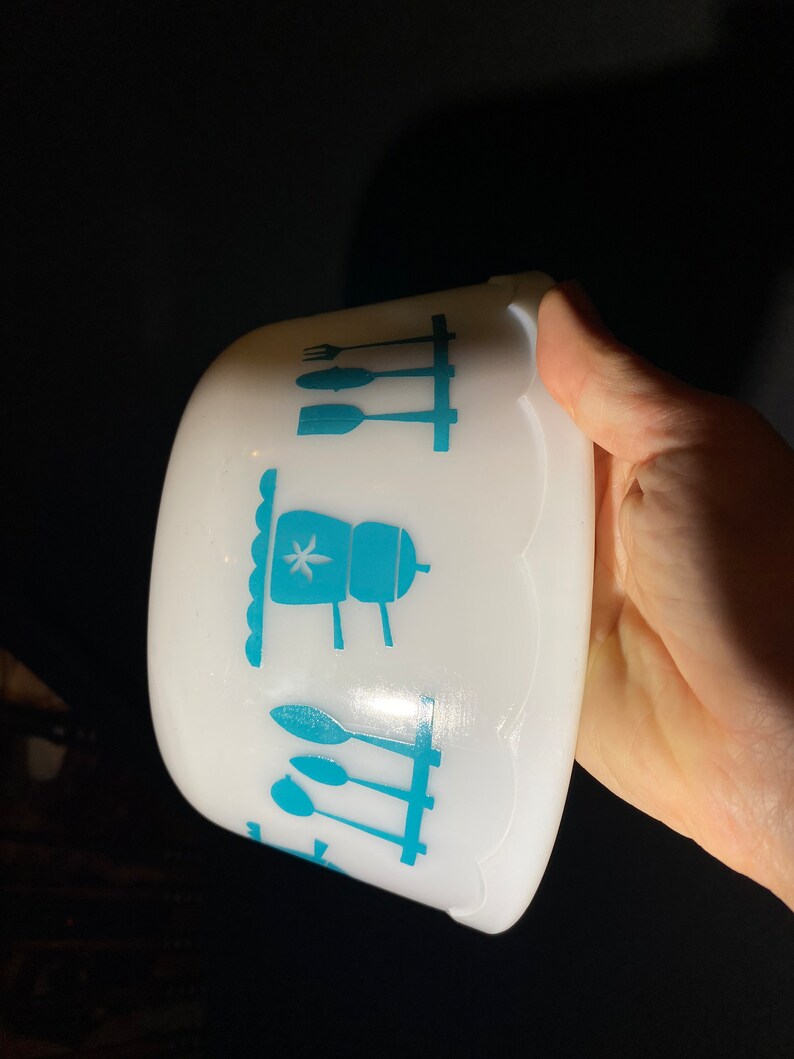 May include: White ceramic bowl with a blue and white kitchen design. The design features a stovetop, utensils, and a star.
