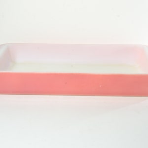Puede incluir: Un molde para hornear de vidrio rosa con un interior blanco. El molde es rectangular y tiene un borde ligeramente redondeado.