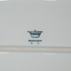 May include: A white rectangular ceramic serving platter with the Thomas Germany logo in dark blue. The logo includes the word "Thomas" above "GERMANY". The platter has a simple, elegant design.