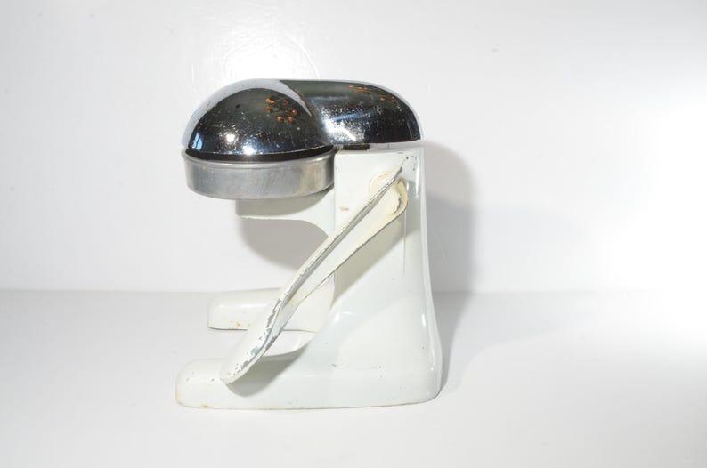 May include: A white and chrome manual citrus juicer with a lever on the side. The juicer is made of metal and has a chrome top.