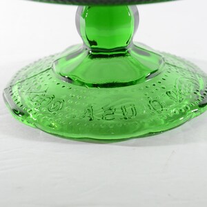 May include: Green glass cake stand with a scalloped edge and a raised design around the base. The base is marked with the words "A 2 U 00".