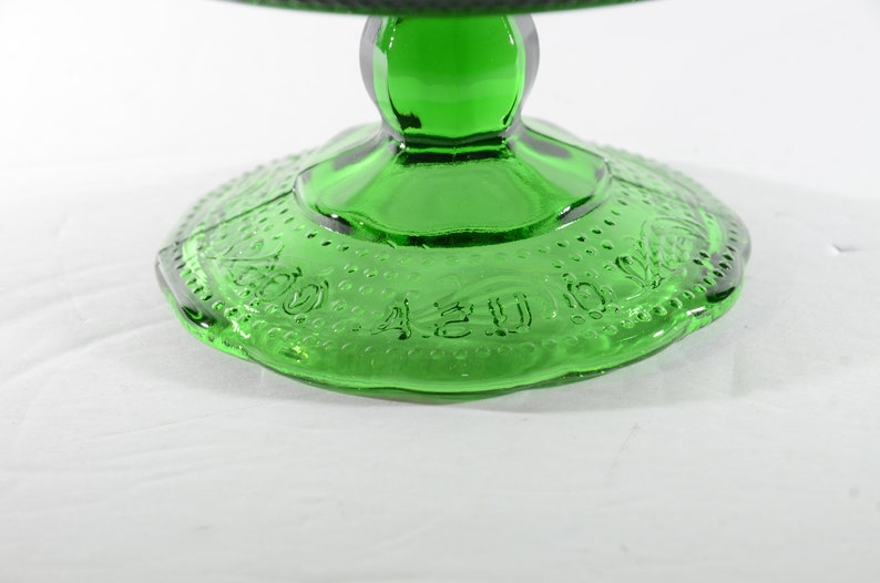 May include: Green glass cake stand with a scalloped edge and a raised design around the base. The base is marked with the words "A 2 U 00".