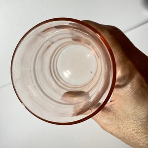 May include: A clear pink glass drinking glass with a rounded bottom and a wide rim. The glass has a smooth, polished surface.