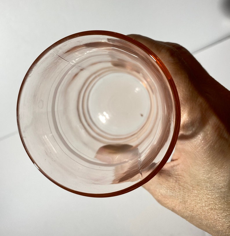 May include: A clear pink glass drinking glass with a rounded bottom and a wide rim. The glass has a smooth, polished surface.