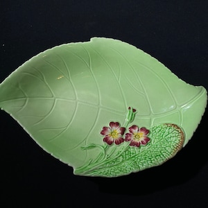May include: A green ceramic leaf-shaped dish with a raised design of a leaf and two pink flowers.