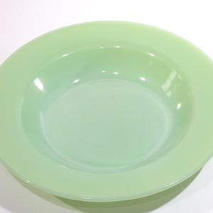 Pode incluir: Uma tigela redonda verde claro com uma borda larga. A tigela tem um acabamento liso e brilhante e é feita de um material sólido e opaco. A tigela tem aproximadamente 25 cm de diâmetro, perfeita para servir saladas ou pratos de massa.