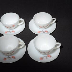 May include: Set of four white ceramic teacups and saucers with a floral design featuring pink flowers and brown stems.